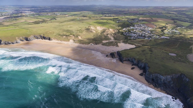 Aerial view of Holywell Bay with waves rolling towards the beach in autumn in Cornwall.